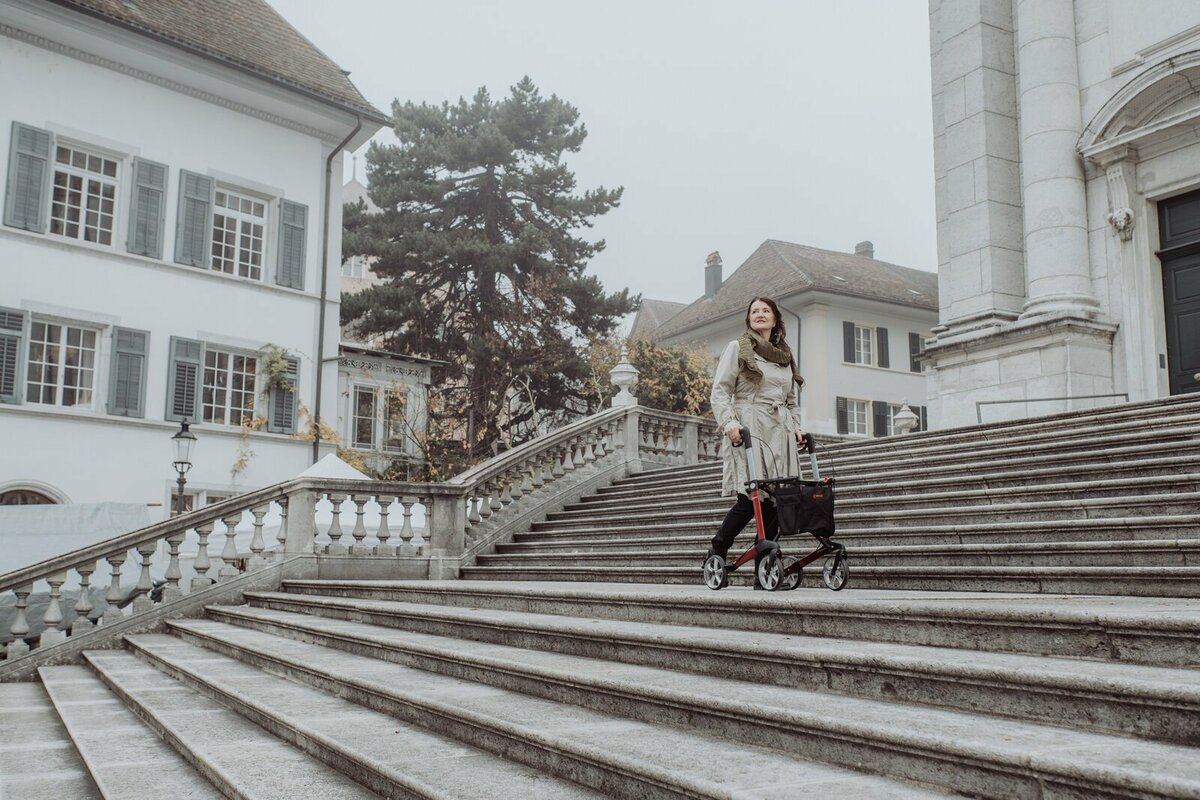 Ältere Person mit dem Rollator unterwegs auf einer Klostertreppe